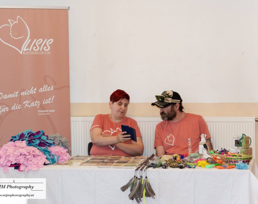 Zwei Personen am Stand von Lisis Katzencouch, umgeben von Spielzeug und Zubehör für Katzen.